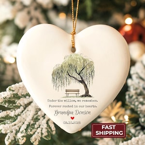 May include: A heart-shaped ceramic ornament with a willow tree design, bench, and text. The text reads "Under the willow, we remember. Forever rooted in our hearts. Grandpa Donson 09.10.2025". The ornament hangs from a gold cord.