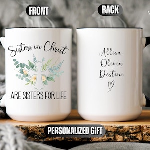 May include: White ceramic mug with a black handle. The front of the mug has a floral design with a cross and the text "Sisters in Christ are sisters for life". The back of the mug has the text "Allisa Olivia Destini" with a heart.