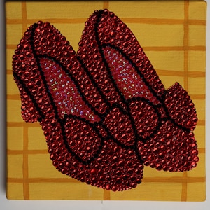 Op de afbeelding: Een paar robijnrode schoenen met zwarte contouren, gemaakt van rode kralen, op een gele achtergrond met een rasterpatroon.
