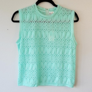 May include: A sleeveless, mint green crochet top with a scalloped pattern. The top has a round neckline and a delicate crocheted trim.