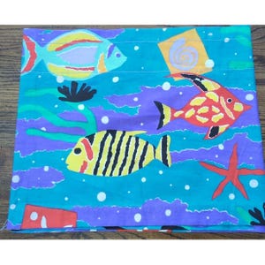 May include: A colorful, patterned fabric featuring an underwater scene. The design includes stylized fish in yellow, red, and blue, along with a red starfish, seaweed, and bubbles. The background is a mix of teal and purple.