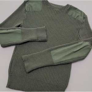 May include: An olive green ribbed knit sweater featuring solid fabric patches on the shoulders and elbows. The long-sleeved garment has a crew neckline and a textured vertical knit pattern throughout the body and sleeves, providing a uniform look.