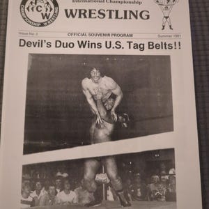 Puede incluir: Portada de programa de recuerdo en blanco y negro para International Championship Wrestling, número 2, verano de 1981. El titular dice "Devil's Duo Wins U.S. Tag Belts!!" con una foto de dos luchadores en el ring.