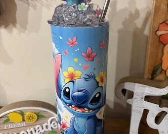 May include: A blue and white stainless steel tumbler with a cartoon Stitch character from Lilo & Stitch. The tumbler has a straw and a small Stitch figurine on top. The tumbler is surrounded by flowers and hearts.