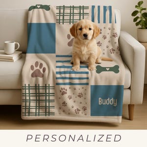 May include: A beige and blue personalized dog blanket with paw prints, plaid, and stripes. A golden retriever puppy sits on the blanket. The blanket has the name "Buddy" printed on it.
