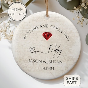 May include: Round ceramic ornament with a vintage background design. It features a red ruby gemstone and the text "40 Years and Counting", "Ruby", "Jason & Susan", and "10.14.1984".