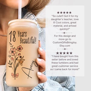 May include: A frosted glass tumbler with a floral design and the text "18 Years Beautiful!" and "Avery". The tumbler has a straw and a lid. The design includes pink flowers and a bow.