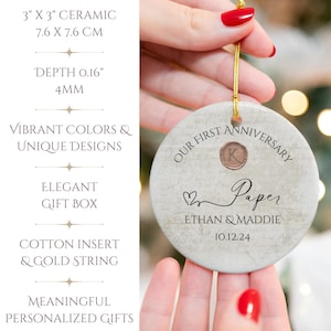 May include: A white ceramic ornament with a marbleized texture. It features the text "Our First Anniversary Paper Ethan & Maddie 10.12.24" and a gold letter "K" in a circle. The ornament is 3 inches in diameter.