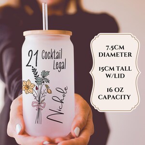 May include: A frosted glass can-shaped tumbler with a bamboo lid and straw. The tumbler features the text "21 Cocktail Legal" and "Nichole", along with a floral bouquet. The tumbler has a 7.5cm diameter, is 15cm tall with the lid, and has a 16 oz capacity.