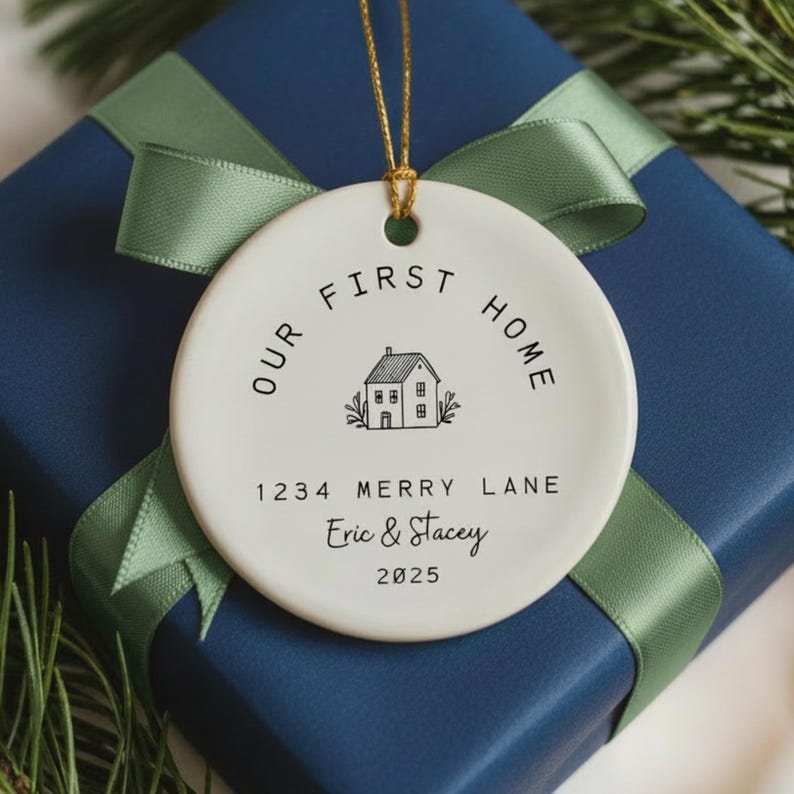 White ceramic ornament with black text that reads 'Our First Home' with a house icon and the address '1234 Merry Lane', names 'Eric & Stacey', and the year '2025'.  The ornament has a string for hanging.  The text 'Ships Fast!' is in the bottom right corner of the image.