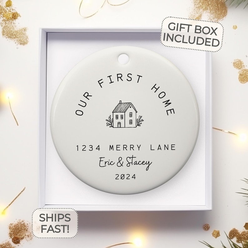 May include: White ceramic ornament with black text that reads "Our First Home" with a house illustration and the text "1234 Merry Lane Eric & Stacey 2024".