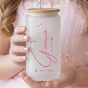 May include: A frosted glass tumbler with a bamboo lid and straw. The tumbler is personalized with the name "Gianna" in pink script, a small heart, and the text "FLOWER GIRL" and "EST. 05-25-2026".