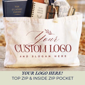 May include: A cream-colored canvas tote bag featuring the maroon text "YOUR CUSTOM LOGO AND SLOGAN HERE" with a small leaf graphic. The bag is filled with a dark blue book titled "THE CLASSIC POEMS," a spiral notebook, a bookmark, and pens.