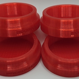 May include: Four bright red, 3D-printed, circular objects. Each object has a cylindrical shape with a slightly flared rim and a recessed interior. The objects are stacked in pairs, with the top objects slightly offset from the bottom ones. The text "NOGOUGER" is visible on the side of each object.