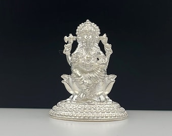Può includere: Statua di Ganesha in argento seduta su una base a forma di loto. La statua è dettagliata e intricata, con un design tradizionale.