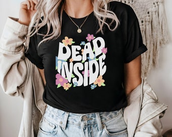 May include: A black t-shirt with a white graphic that says "DEAD INSIDE" in a retro font with colorful flowers surrounding the text.