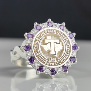 May include: A silver ring with a purple and white stone setting. The ring features a circular design with the words "Tarleton State University" and "Stephenville, Texas" around the edge. The center of the ring features a stylized "T" inside a circle.