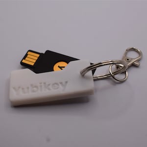 May include: A white Yubikey security key with a black USB connector attached to a silver keyring. The Yubikey is a small, portable device that can be used to secure online accounts.