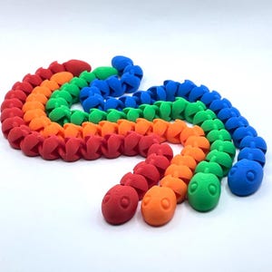 May include: A vibrant, segmented toy in a rainbow of colours: red, orange, green, and blue. The toy is made of connected, rounded segments, creating a flexible, snake-like form. The segments have a textured surface.