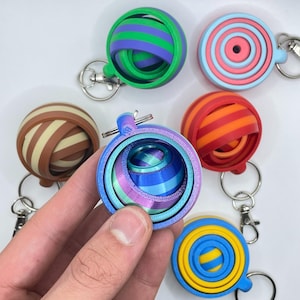 May include: A set of six colourful, layered, sphere-shaped keyrings. Each keyring is made of plastic and features a different colour combination of stripes. The keyrings are all attached to silver key rings.