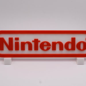 May include: A red and white plastic sign with the word "Nintendo" in white letters. The sign is on a white stand.