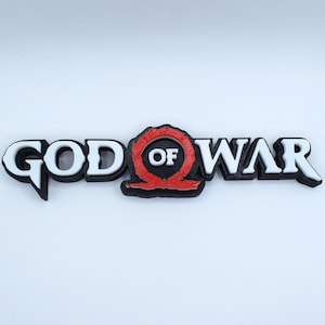 May include: A 3D printed logo for the video game God of War. The logo is white with black outlines and features the game's iconic symbol, a red circle with a black axe inside, with the words "God of War" written in white.