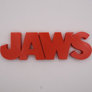 May include: A red 3D printed word "JAWS" with a textured surface.
