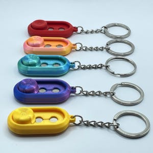 May include: Five fidget spinner keychains in various colours: red, rainbow, blue-green, purple-blue, and yellow. Each has a circular spinner and two holes, connected to a silver chain and keyring. A fun and practical accessory for keys.