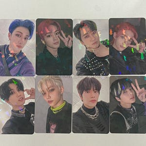 Pode incluir: Um conjunto de dez cartões de fotos com diferentes membros de uma banda de meninos. Cada cartão tem um membro diferente com um fundo colorido e um efeito holográfico.