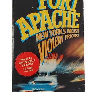 May include: A book cover with a yellow and blue title "FORT APACHE" and the text "NEW YORK'S MOST VIOLENT PRECINCT". The cover features a blurred image of a police car with red and orange lights. The book is by Tom Walker.