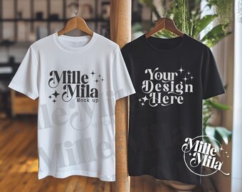 May include: Two t-shirts hanging on wooden hangers. The white t-shirt has the text "Mille Mila" and "Mock up" printed on it. The black t-shirt has the text "Your Design Here" printed on it.