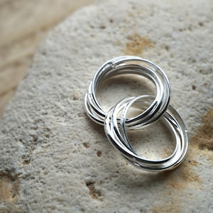 Peut inclure: Un ensemble de cinq anneaux en argent entrelacés. Les anneaux sont lisses et brillants, et ils sont disposés en cercle.