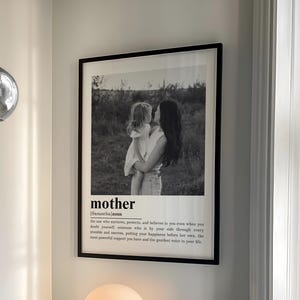 May include: A bedroom scene featuring a bed with light blue bedding, a framed black and white print with the word "mother", and a spherical pendant light. A small, round lamp sits on a nightstand. Bookshelves are visible in the background.