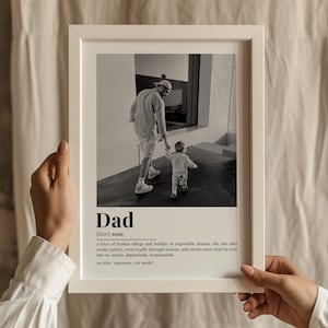 May include: A white framed print with a black and white photograph of a father and child. The print has the word "Dad" and a definition. The frame is white.