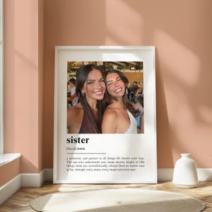 Pu&ograve; includere: Una stampa incorniciata con una fotografia di due donne sorridenti. La parola "sister" e una definizione sono stampate sotto. La cornice &egrave; bianca e lo sfondo &egrave; di un caldo color pesca.