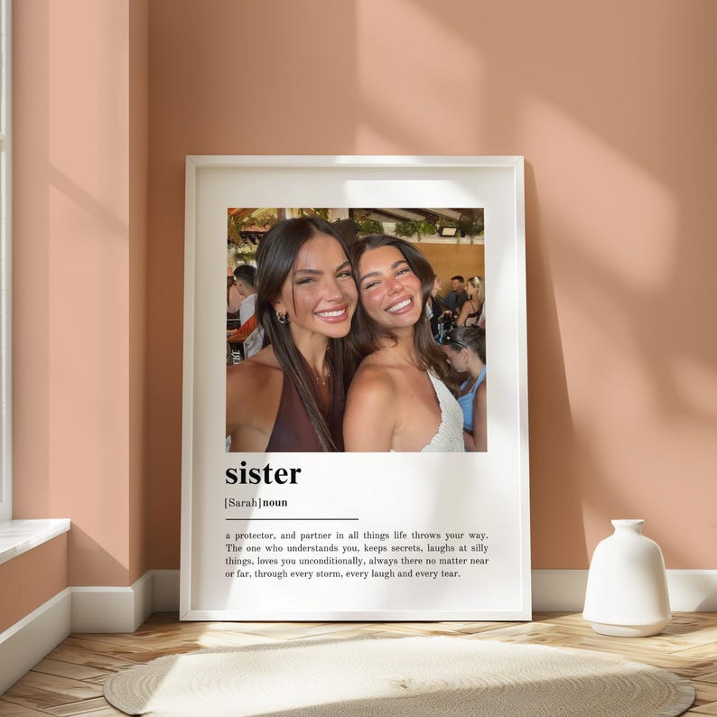 Pu&ograve; includere: Una stampa incorniciata con una fotografia di due donne sorridenti. La parola "sister" e una definizione sono stampate sotto. La cornice &egrave; bianca e lo sfondo &egrave; di un caldo color pesca.