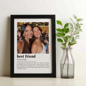 Puede incluir: Un cuadro con marco negro que contiene una fotograf&iacute;a de dos personas sonrientes. Debajo de la imagen, el texto dice best friend [Natalie] noun, seguido de una definici&oacute;n que describe a un alma irremplazable que ama incondicionalmente.