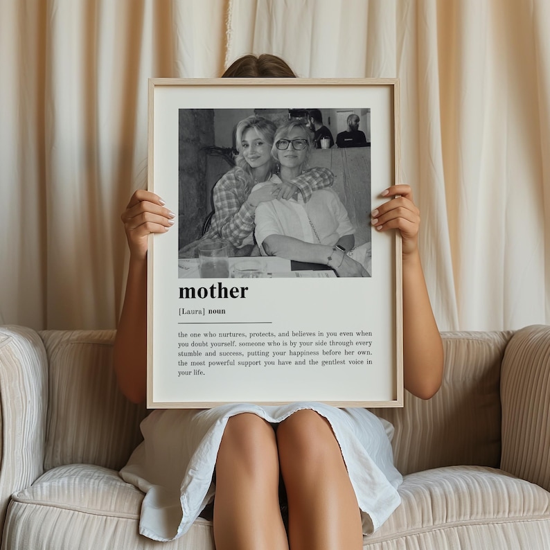 May include: A framed black and white print featuring a photograph of two women embracing. The print includes the word "mother" with a definition below. The frame is light-colored.