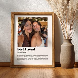 Puede incluir: Una impresi&oacute;n art&iacute;stica enmarcada que presenta una fotograf&iacute;a de dos personas sonrientes sobre la definici&oacute;n de diccionario del t&eacute;rmino best friend, incluido el nombre Natalie, impresa en texto negro sobre fondo blanco en un marco de madera.