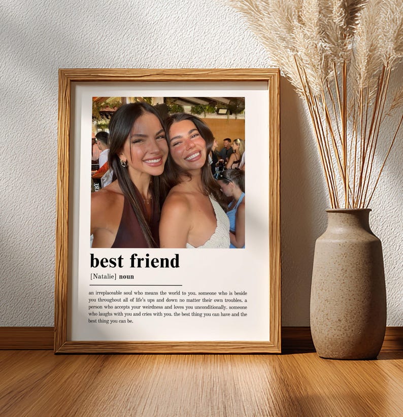 Puede incluir: Una impresi&oacute;n art&iacute;stica enmarcada que presenta una fotograf&iacute;a de dos personas sonrientes sobre la definici&oacute;n de diccionario del t&eacute;rmino best friend, incluido el nombre Natalie, impresa en texto negro sobre fondo blanco en un marco de madera.