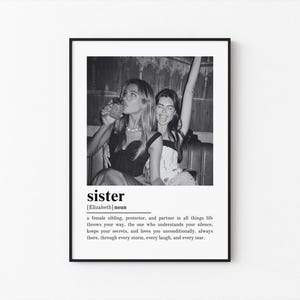 May include: Black and white framed print featuring a photograph of two women. One is drinking from a glass, the other has her arm raised. The word "sister" is printed below the photo, along with a definition.