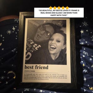Puede incluir: Un marco de fotos de madera negra que contiene una fotograf&iacute;a en blanco y negro de dos personas sonriendo. Debajo de la foto, el texto dice: best friend [Amber] noun, seguido de una definici&oacute;n. Una rese&ntilde;a de cinco estrellas es visible.