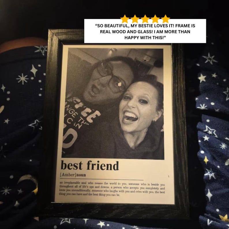 Puede incluir: Un marco de fotos de madera negra que contiene una fotograf&iacute;a en blanco y negro de dos personas sonriendo. Debajo de la foto, el texto dice: best friend [Amber] noun, seguido de una definici&oacute;n. Una rese&ntilde;a de cinco estrellas es visible.
