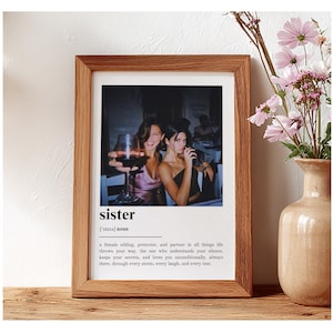Pu&ograve; includere: Una stampa incorniciata con una cornice in legno. La stampa presenta una foto di due donne, una delle quali tiene in mano un bicchiere di vino rosso. La parola "sister" &egrave; stampata sotto la foto, insieme a una definizione.