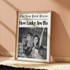 May include: A framed black and white print designed to look like a newspaper front page. The headline reads "How Lucky Are We" with the text "Your Photo Goes Here" below a photo of two women. The newspaper is titled "The New York Press".
