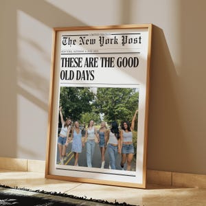 Puede incluir: Una impresión enmarcada con un diseño de periódico, que muestra el titular "THESE ARE THE GOOD OLD DAYS". La sección superior dice "The New York Post" y "LIMITED EDITION". La imagen de abajo muestra a un grupo de mujeres caminando por una carretera. El marco es de color marrón claro.