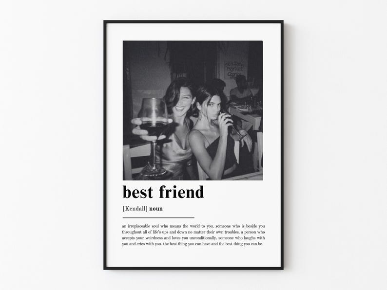 Puede incluir: Una l&aacute;mina de arte mural enmarcada en blanco y negro que presenta una definici&oacute;n de estilo diccionario del t&eacute;rmino best friend con el sustantivo Kendall debajo y una fotograf&iacute;a de dos personas sosteniendo copas de vino en una mesa sobre el texto.