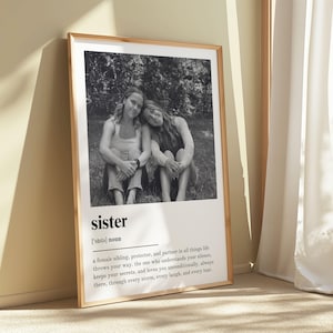 Pu&ograve; includere: Una stampa in bianco e nero incorniciata con due persone sedute insieme, con la parola "sister" e la sua definizione sottostante. La definizione descrive una sorella, protettrice e partner.
