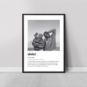 Pu&ograve; includere: Stampa incorniciata in bianco e nero con due persone in maglione, una delle quali tiene una macchina fotografica. La parola "sister" &egrave; visualizzata con una definizione sottostante. La stampa &egrave; esposta su un muro bianco.