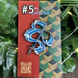 May include: A pin featuring a blue and white wave design with a sword, set against a red and geometric patterned background. The pin is labelled with the number 5 and the name "Giyuu Tomioka".